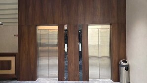 Un juego de puertas dobles con un panel de madera vertical en el centro, un bote de basura a la derecha y parte de una pared con un letrero.