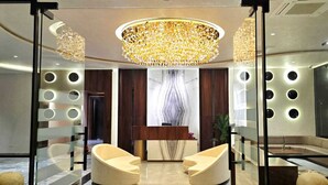 Un vestíbulo moderno con un mostrador de recepción de mármol, dos sillones color beige, una lámpara de araña grande y luces circulares en la pared.