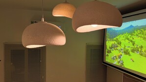 A room with three pendant lights, a large TV screen displaying a landscape, and two windows with blinds. - Best Location | Home Cinema | Peaceful | Calmigo (Thành phố Hồ Chí Minh)