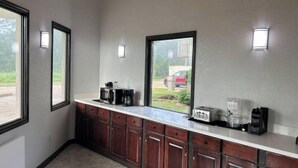 Una cocina con microondas, tostadora y cafetera en la encimera, armarios de madera y un ventanal con vista a un coche rojo afuera.