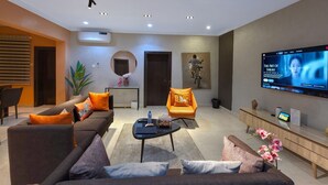 Un salon moderne comprenant un canapé, des fauteuils, une table basse et un téléviseur à écran plat fixé au mur.