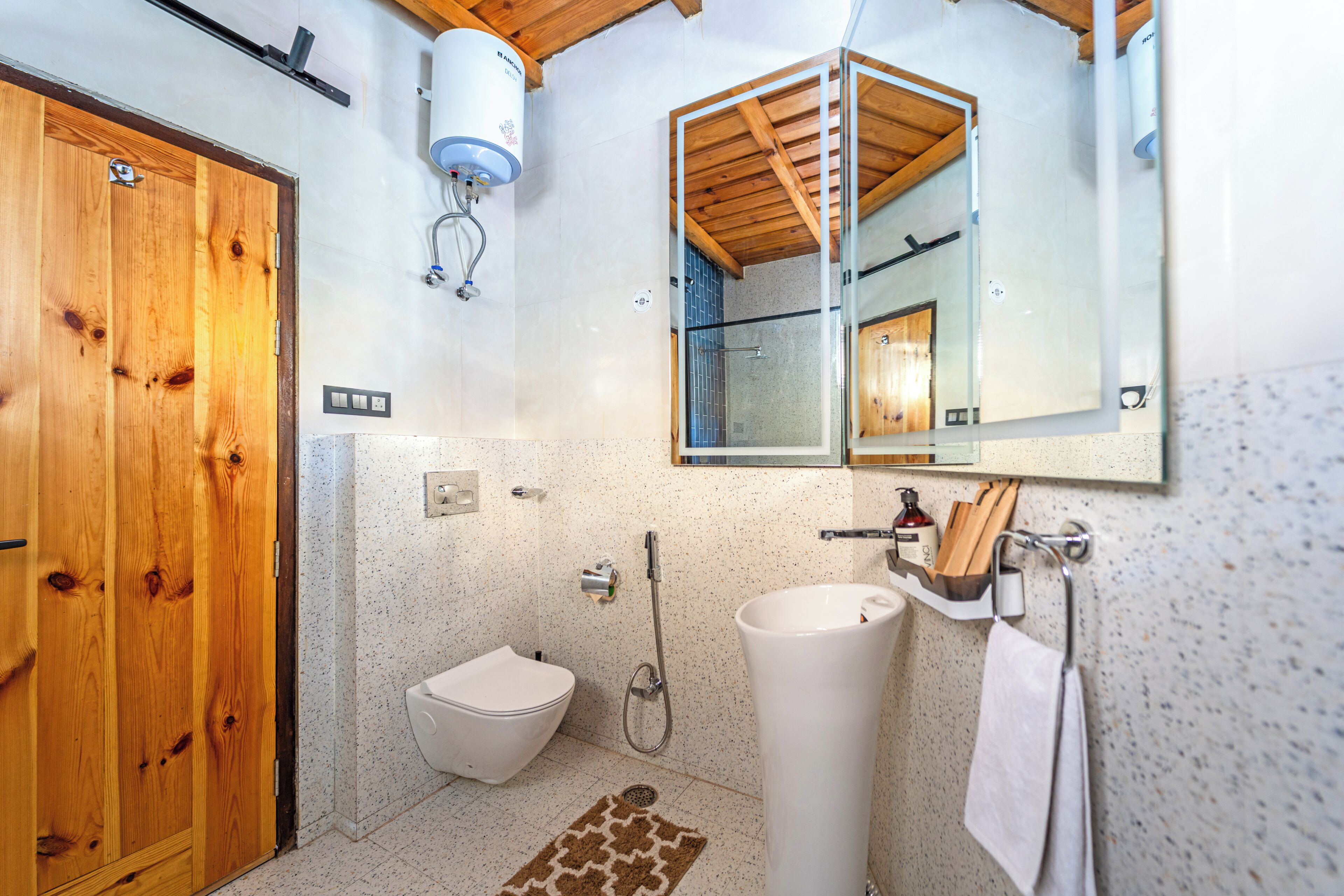 A bathroom with a wooden door, a toilet, a sink, a shower, and a mirror.