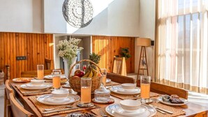 Une table à manger dressée avec des assiettes, des verres et un panier de fruits.