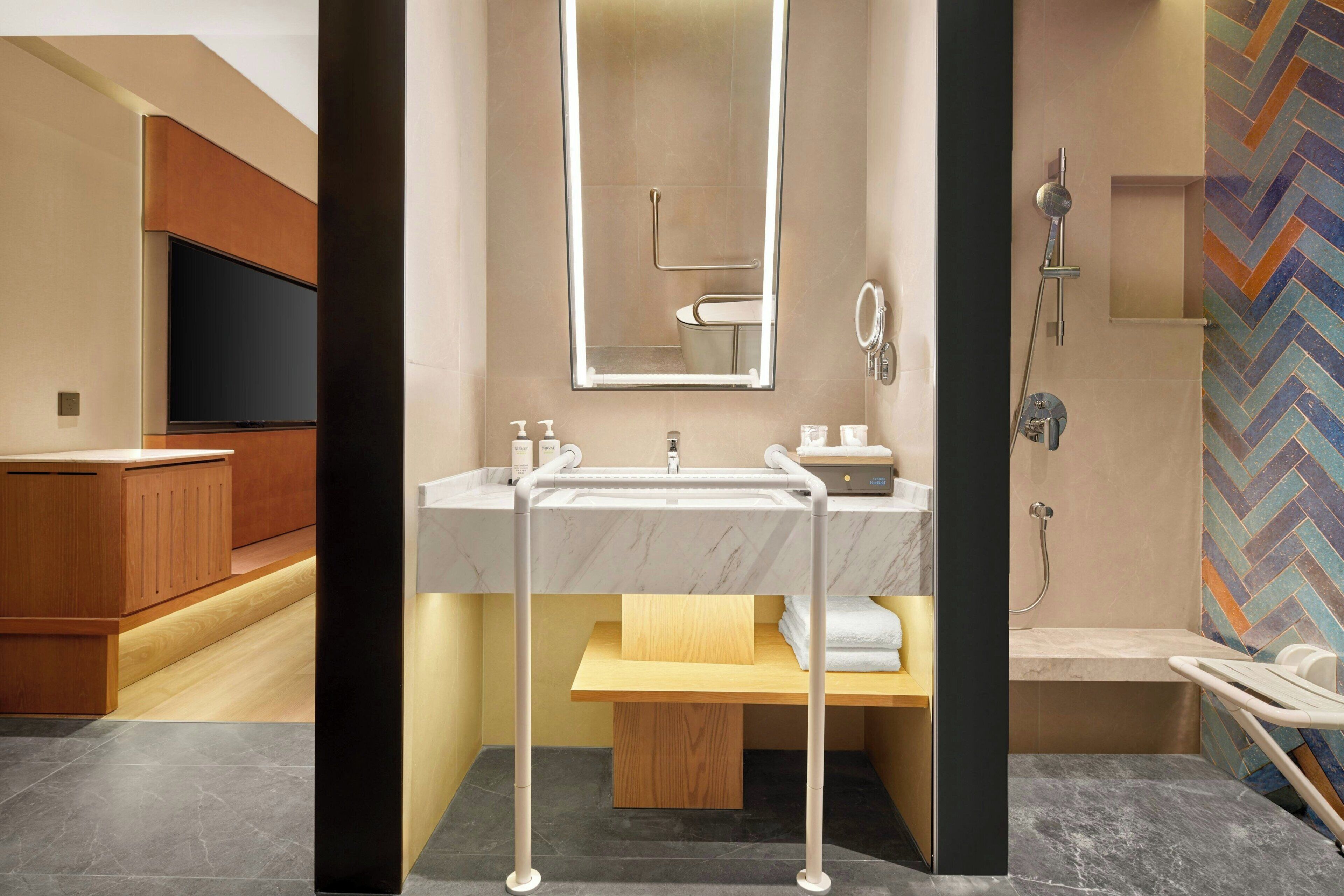 A modern bathroom with a marble sink, a mirror, a shower, and a wooden vanity.