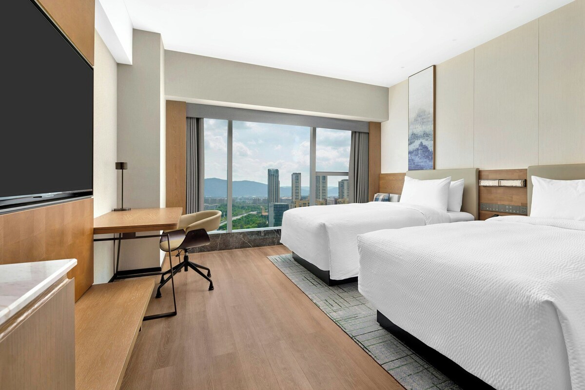 A hotel room with two beds, a desk, and a chair.