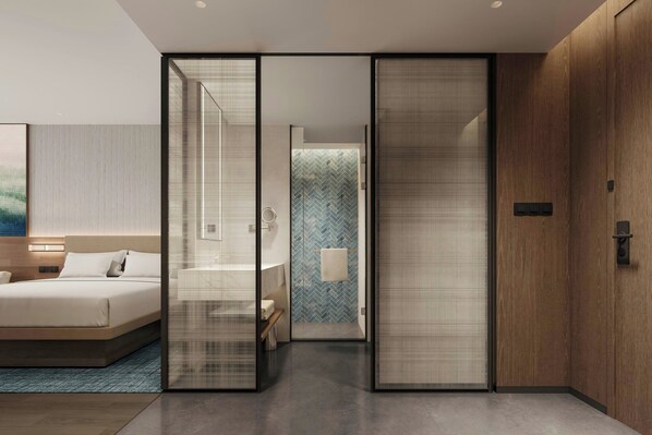A modern hotel room with a bed, a bathroom, and a sliding door leading to another room.