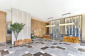 Un moderno vestíbulo de hotel con un mostrador de recepción, una silla verde, una planta y una pared decorativa con diseño de cuadrícula.