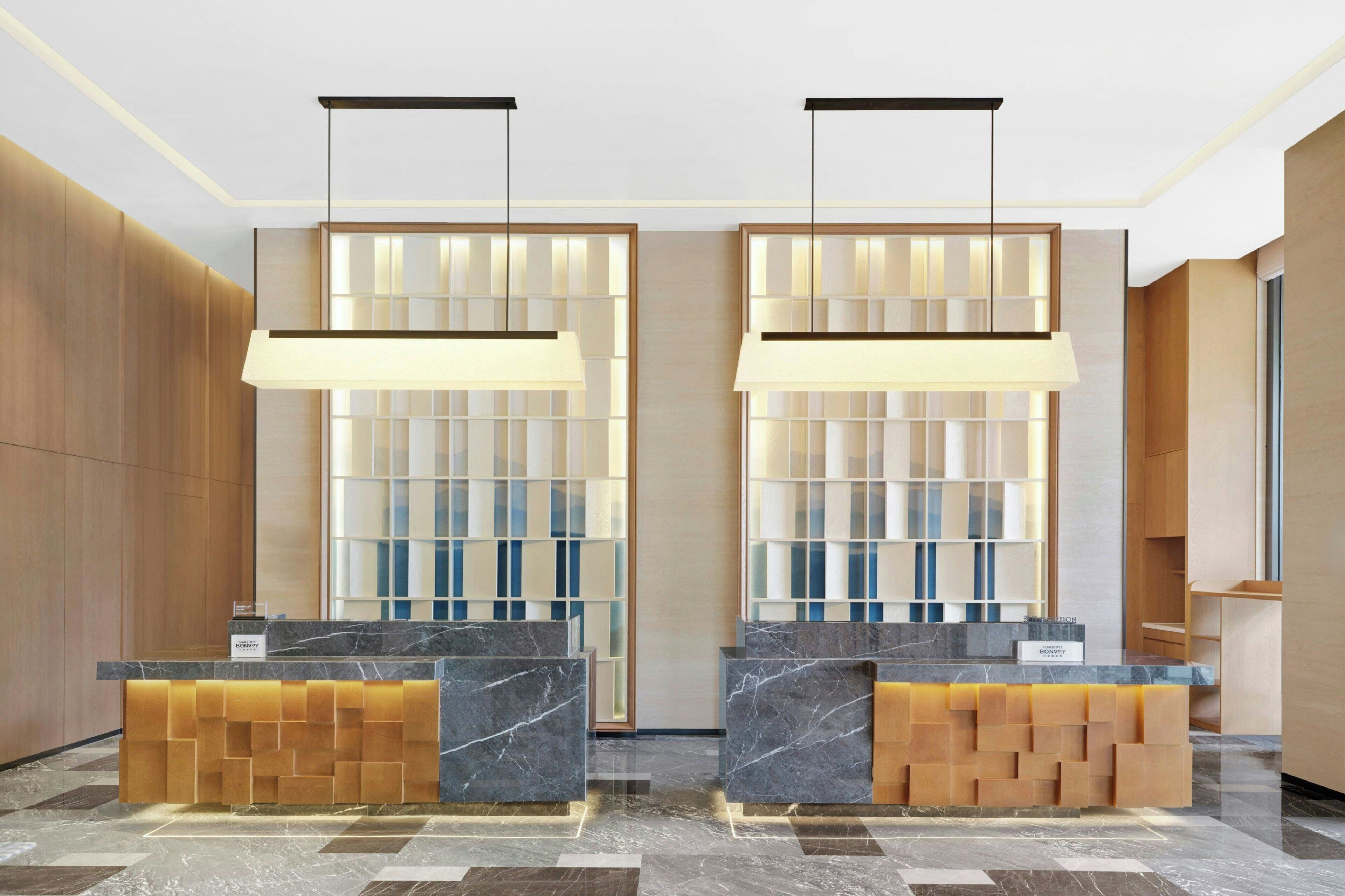 A hotel reception area with marble counters, wooden paneling, and a modern light fixture.