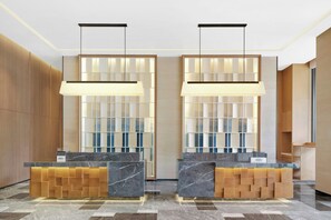 Een hotel receptie met marmeren balies, houten lambrisering en een moderne lamp.