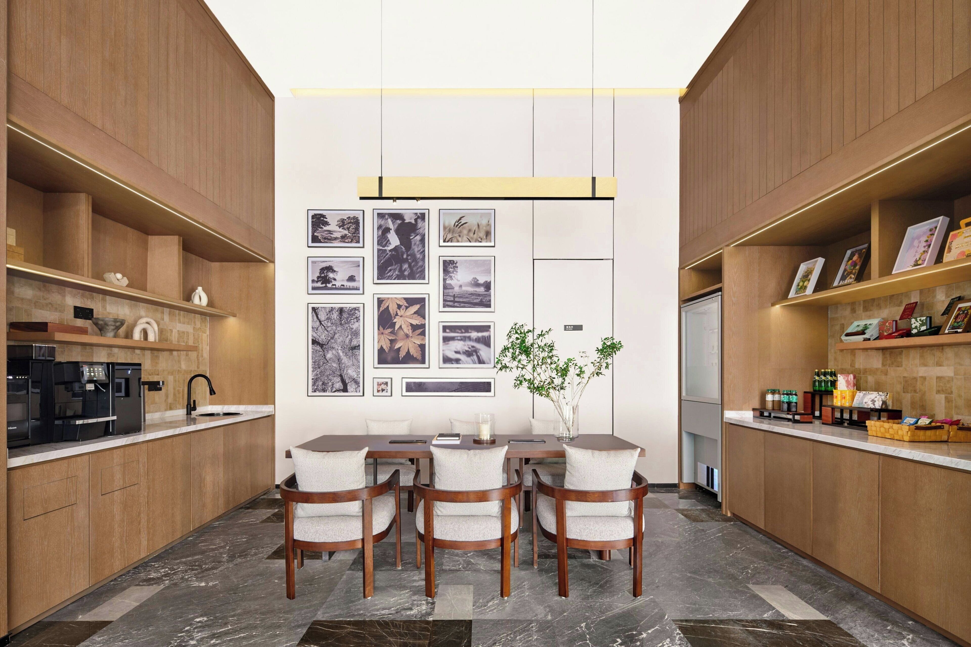 A modern kitchen with a dining area, featuring a central island, wooden cabinets, and a wall adorned with framed pictures.