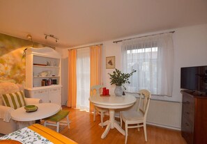 A cozy living room with a round dining table, a sofa, a television, and a bookshelf.