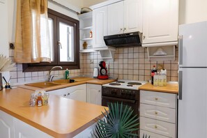 Una cocina con armarios blancos, estufa, fregadero y una ventana con cortinas.