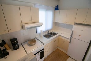 Eine kleine Küche mit weißen Schränken, einem Backofen, einer Spüle und einem Kühlschrank.