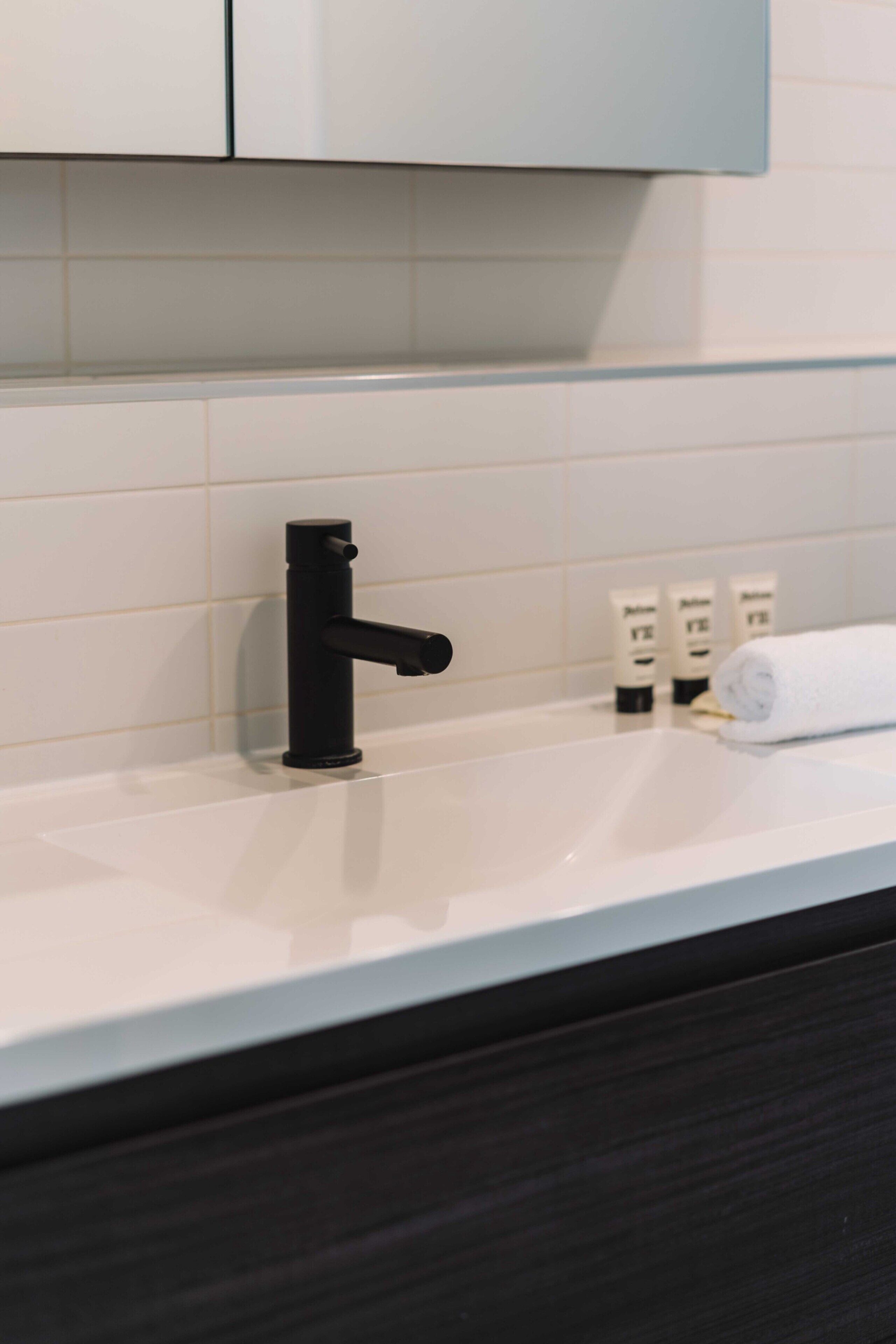 A bathroom with a black faucet, white tiles, and toiletries on the counter.