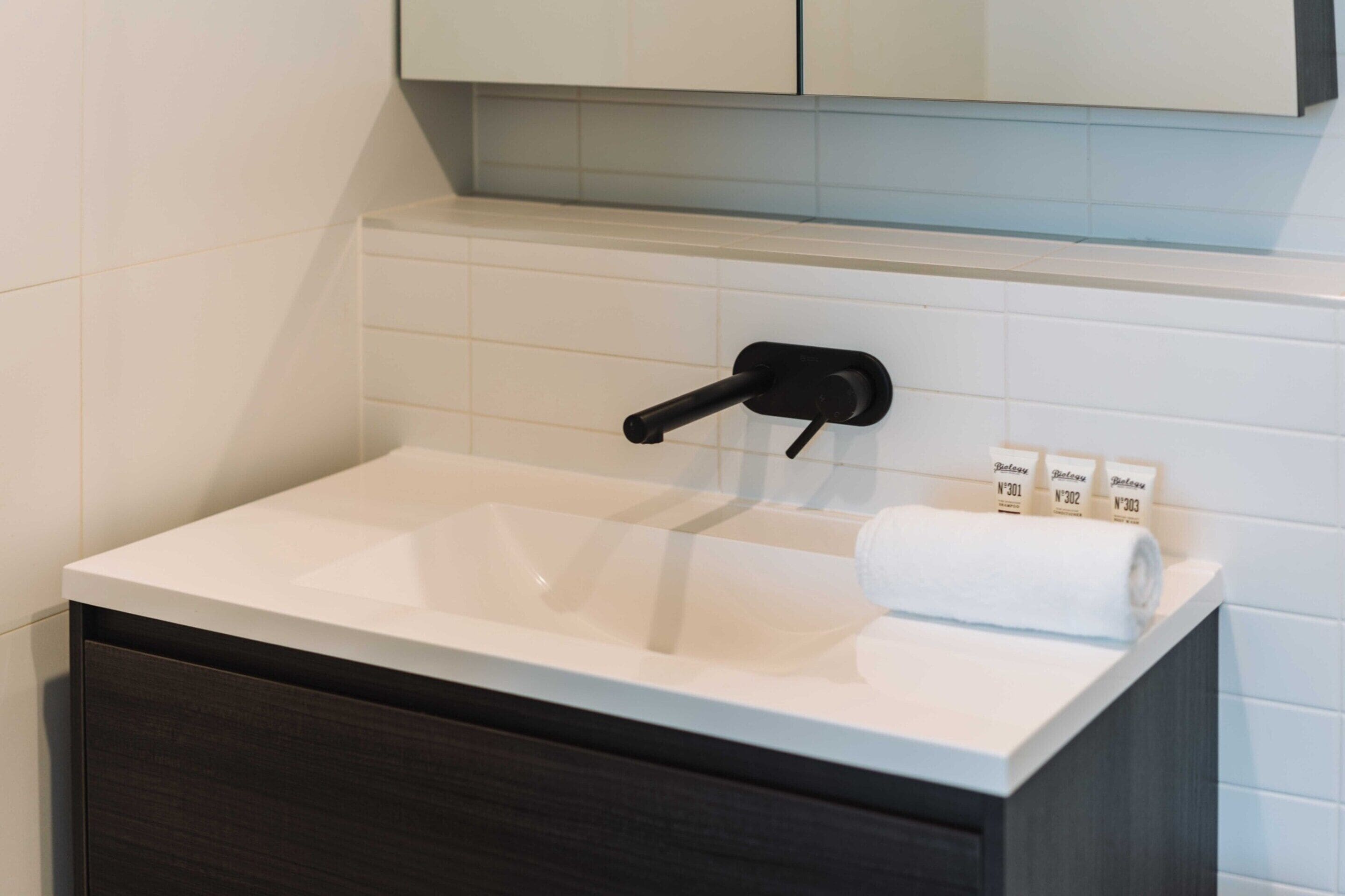 A bathroom with a white sink, dark cabinet, and a towel dispenser.