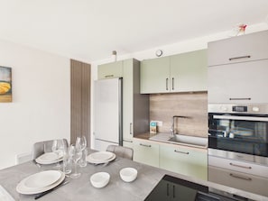 A modern kitchen with a dining area, stainless steel appliances, and a minimalist design. - Apartment for 3, 100m from the beach (St-Brévin-l’Océan)
