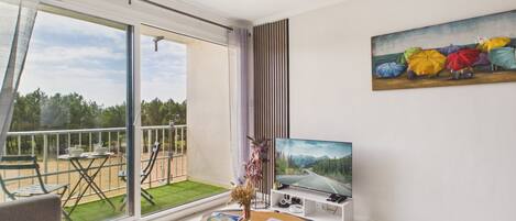 A modern living room with a large sliding glass door leading to a balcony, a flat-screen TV, and a painting on the wall.