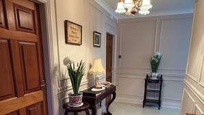 Un couloir avec une porte en bois, une lampe, une petite table sur laquelle se trouve une statue, un tapis et un lustre.