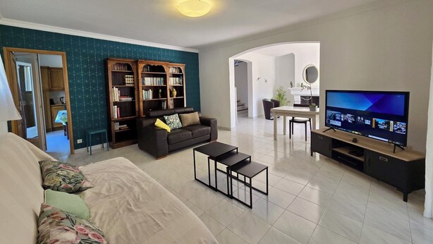Een woonkamer met een bank, salontafel, televisie, boekenkast en een eethoek.