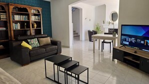 Een woonkamer met een bank, salontafel, televisie, boekenkast en een eethoek met tafel en stoelen.