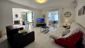 Een woonkamer met een bank, televisie en een eethoek met een tafel en stoelen.