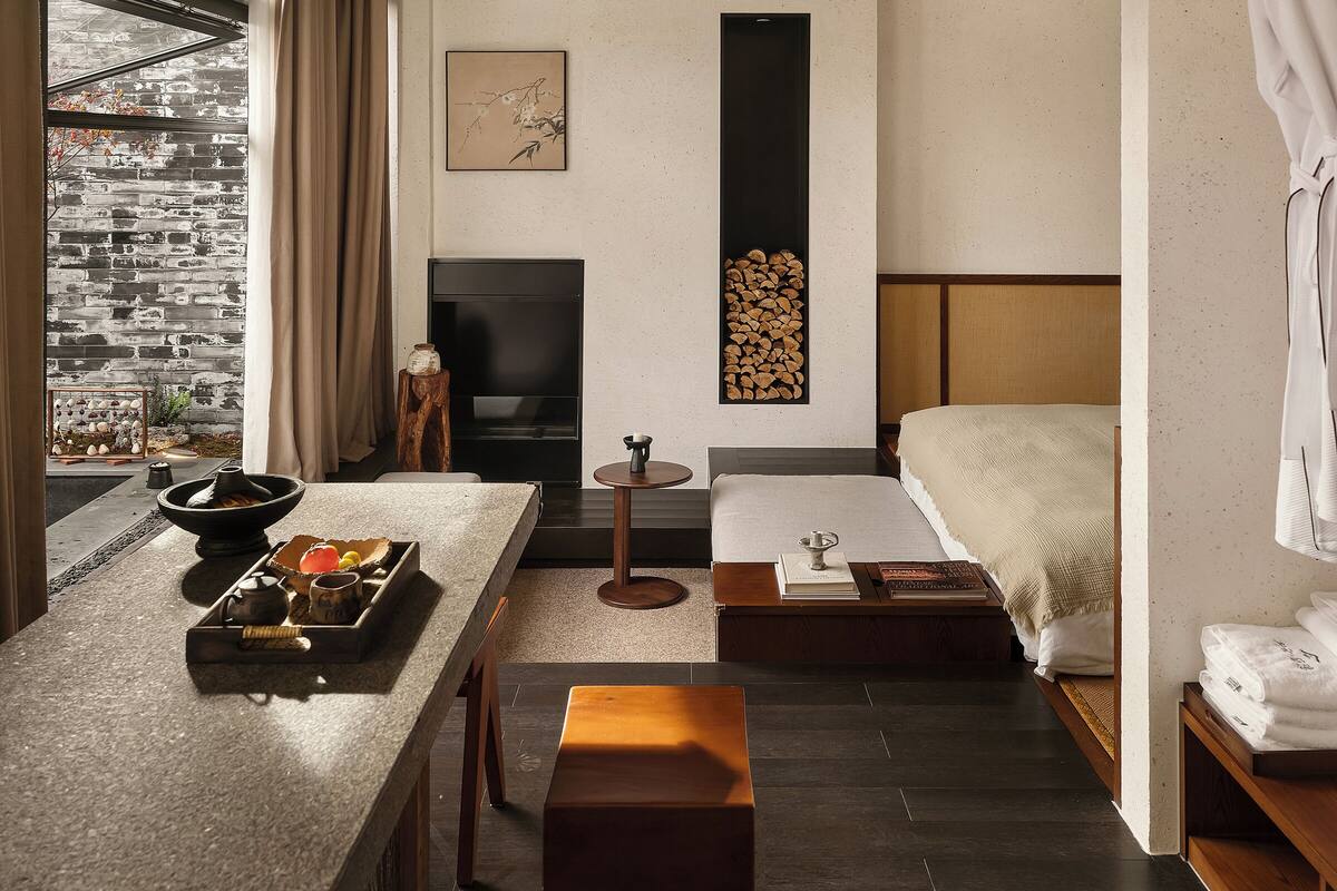 A modern room with a stone counter, a bed, a fireplace, and a view of a mountain.