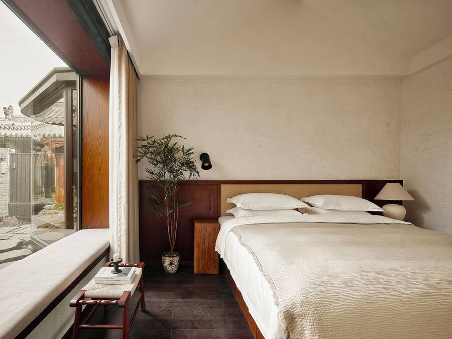 Habitación de hotel con cama, mesita de noche, lámpara y vistas a un edificio tradicional.