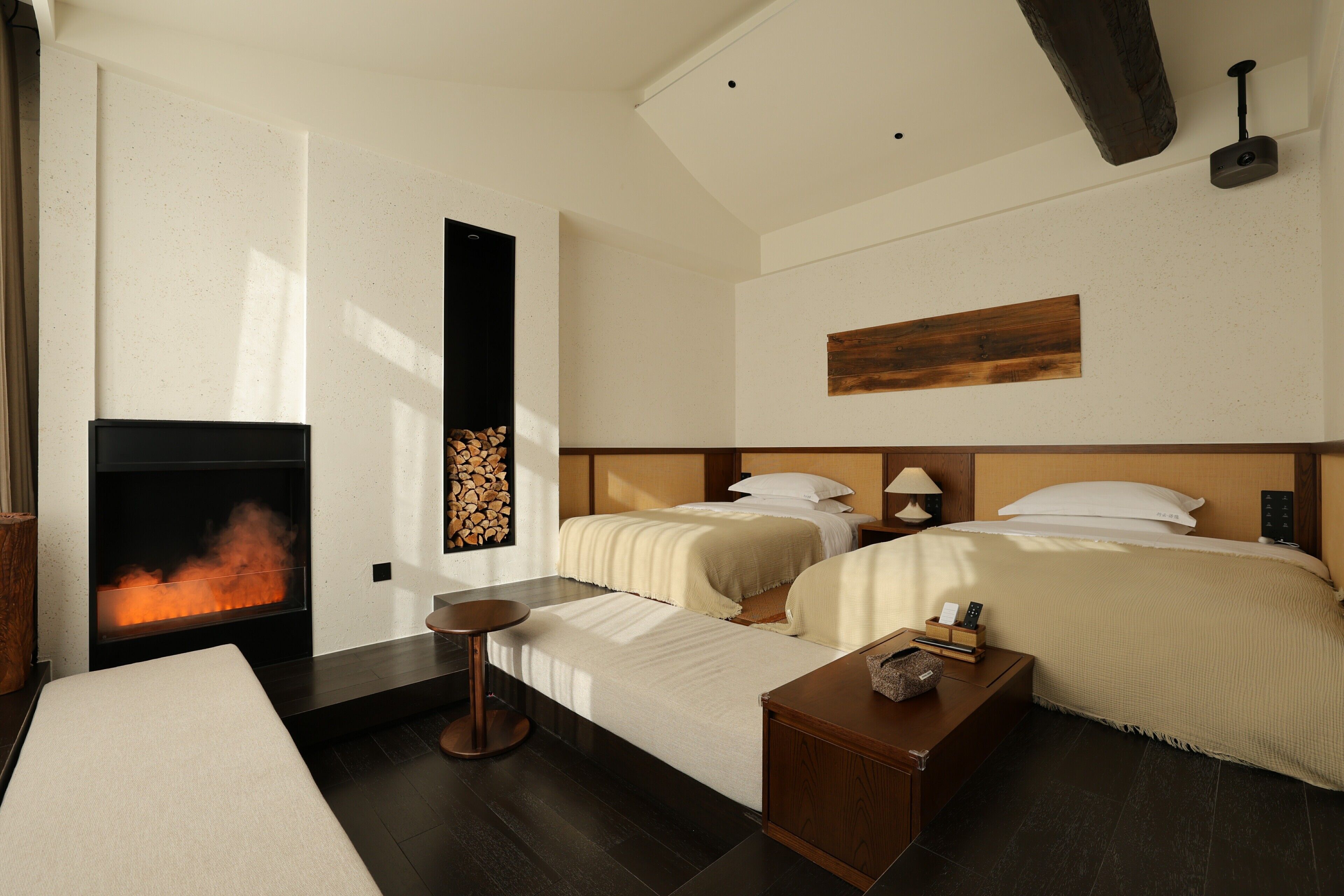 A hotel room with a fireplace, two beds, a small table, and a bedside lamp.