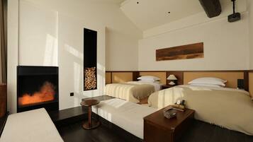 A hotel room with a fireplace, two beds, a small table, and a bedside lamp.