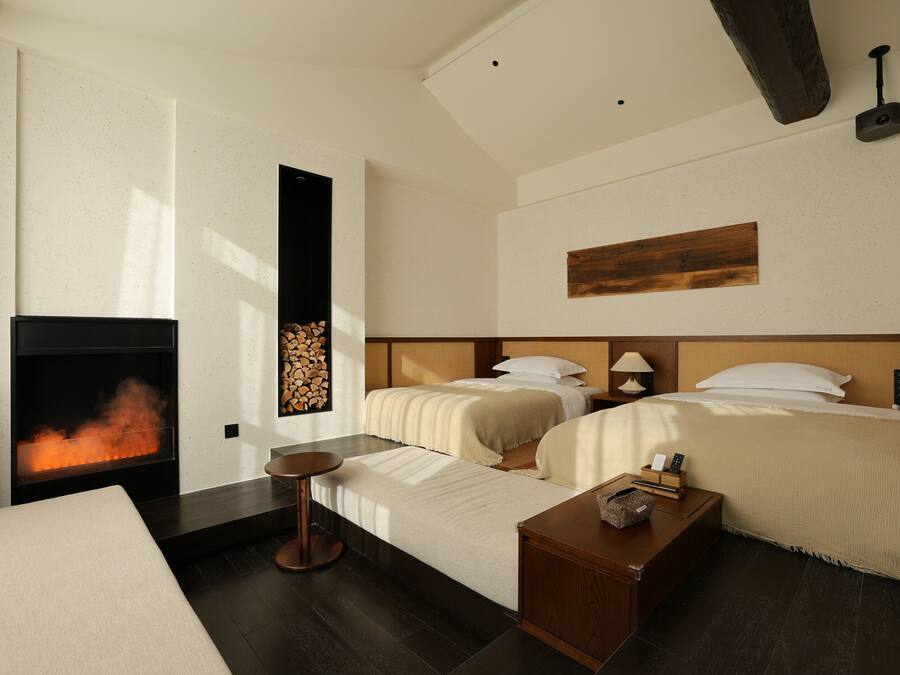 A hotel room with a fireplace, two beds, a small table, and a bedside lamp.