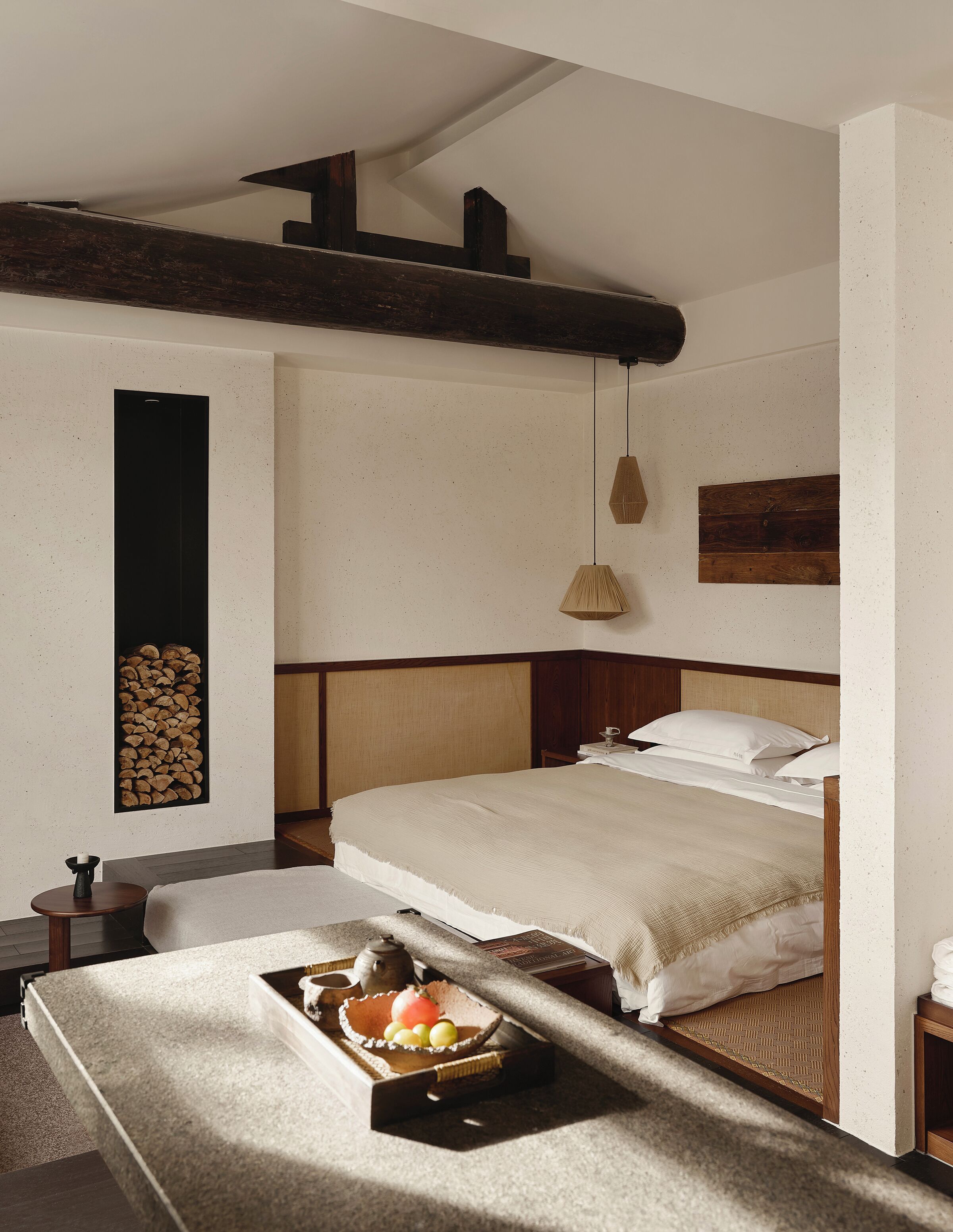 A bedroom with a bed, bedside table, lamp, and a wall-mounted shelf with logs.