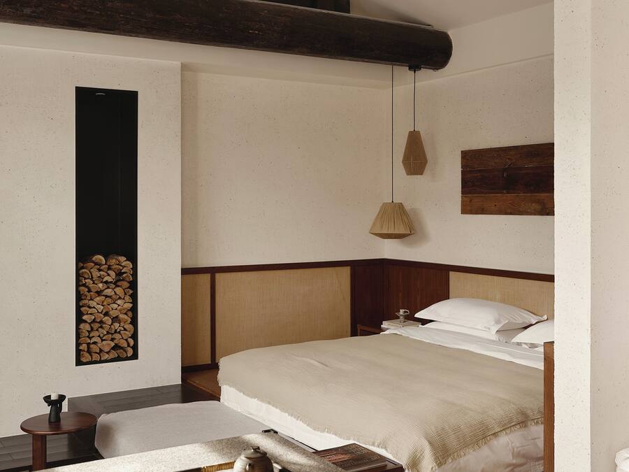 A bedroom with a bed, bedside table, lamp, and a wall-mounted shelf with logs.