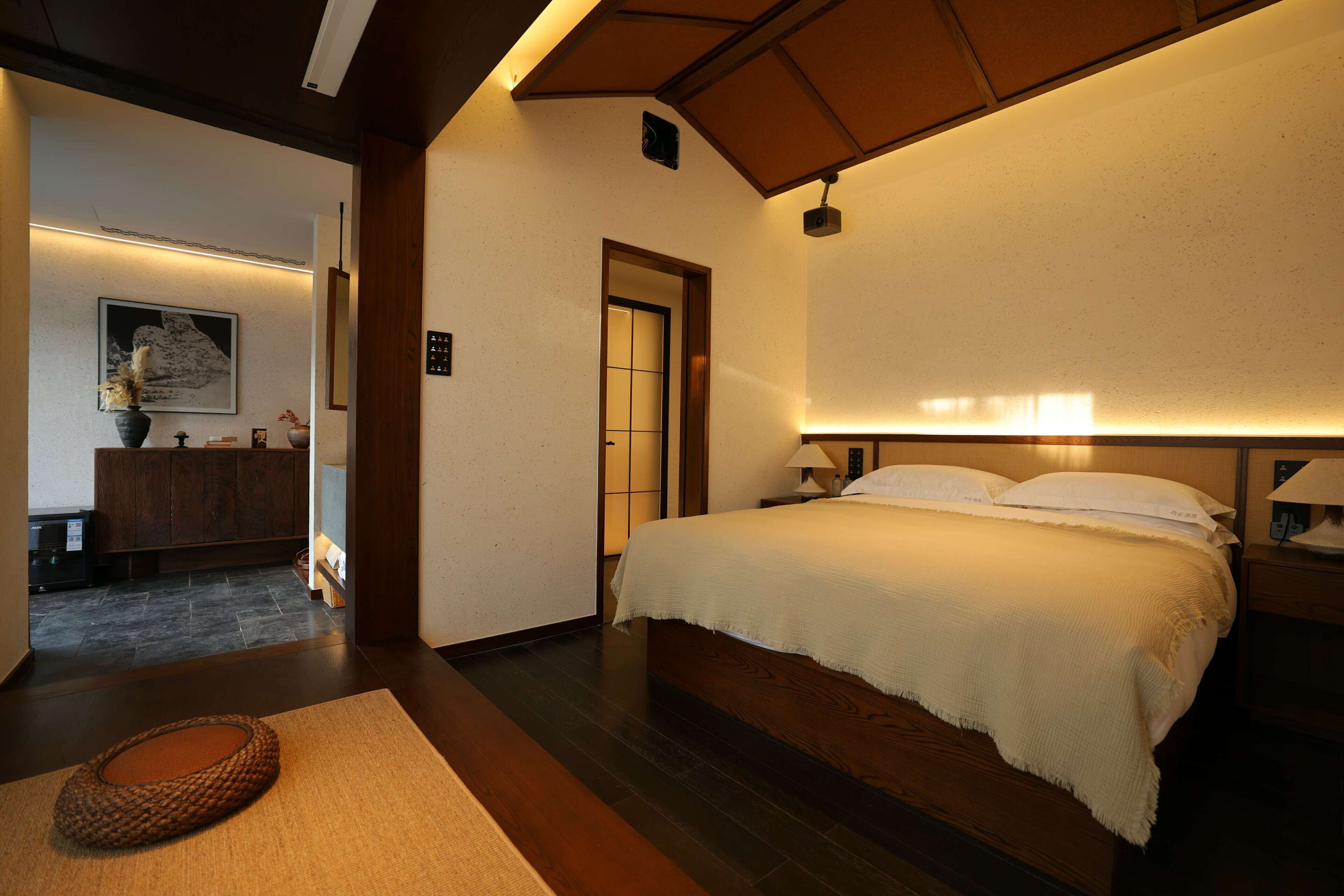 Una habitación de hotel con una cama grande, piso de madera, una alfombra pequeña y una mesita de noche con una lámpara.