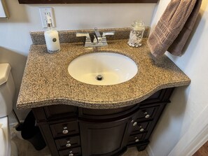 A bathroom with a granite countertop, a white sink, dark wooden cabinets, a towel rack, and a soap dispenser. - Serene and Comfortable Suburban Hideaway (Lower Sackville)