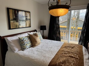 A bedroom with a bed, a painting, a lamp, and a view of a balcony. - Serene and Comfortable Suburban Hideaway (Lower Sackville)