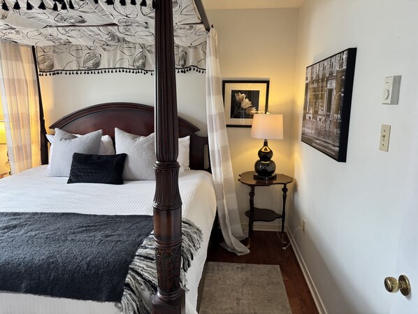 A four-poster bed with a canopy, a bedside table with a lamp, a framed picture on the wall, and a door with a handle. - Serene and Comfortable Suburban Hideaway (Lower Sackville)