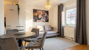 Ein modernes Wohnzimmer mit Essbereich, einer Chandelieber, einer Couch und einem großen Fenster mit Vorhängen.