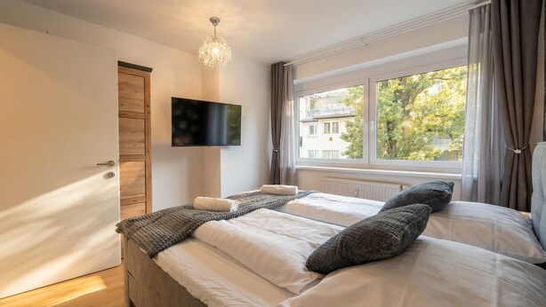 Ein Schlafzimmer mit einem Bett, einem Fernseher, einem Fenster mit Vorhängen und einer Holztür.