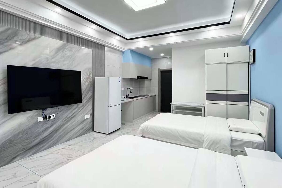 A modern hotel room with a flat-screen TV, a kitchenette, a bed, and a wardrobe.