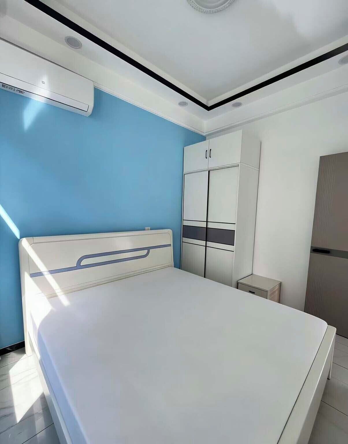 A bedroom with a bed, wardrobe, and a small bedside table.