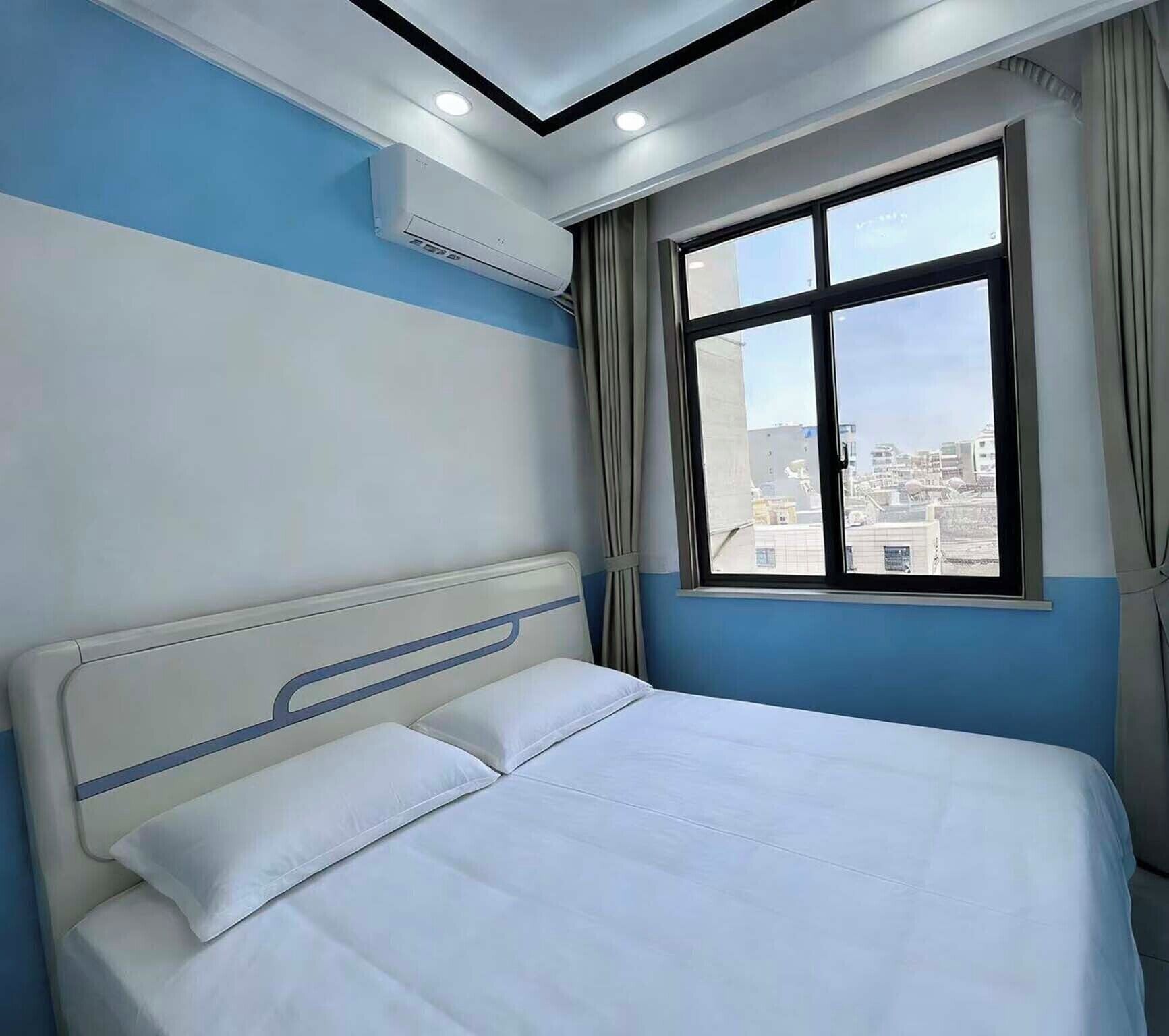 A hotel room with a bed, a window with curtains, and an air conditioning unit.