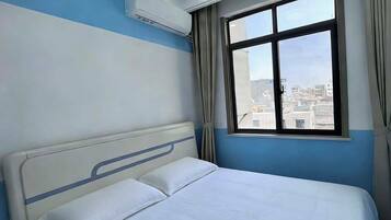 A hotel room with a bed, a window with curtains, and an air conditioning unit.