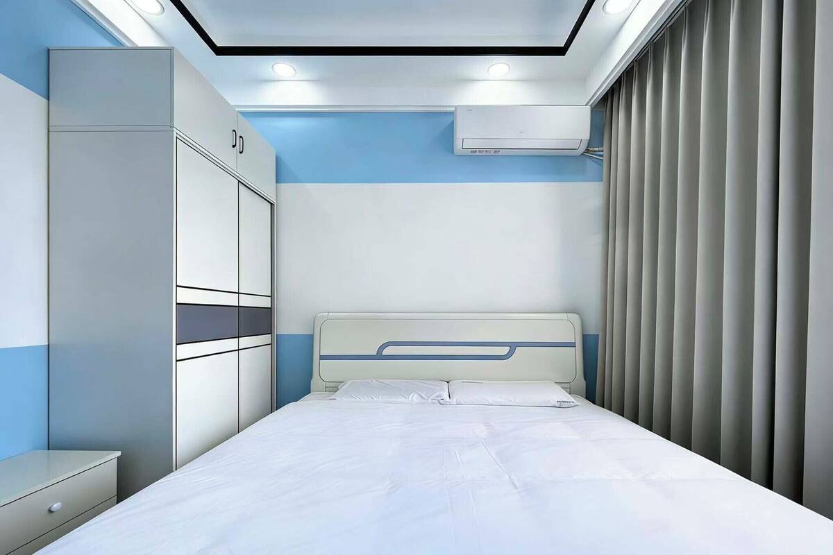 A bedroom with a bed, a wardrobe, a nightstand, an air conditioning unit, and a curtain.