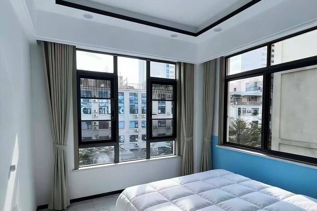 A bedroom with a bed, large windows, and a view of buildings outside.