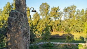 Estructura de piedra con una lámpara de metal, rodeada de follaje y árboles.