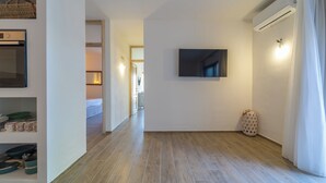 Un pasillo con una televisión de pantalla plana montada en la pared, un pequeño cubo de basura y una puerta con un equipo de aire acondicionado.