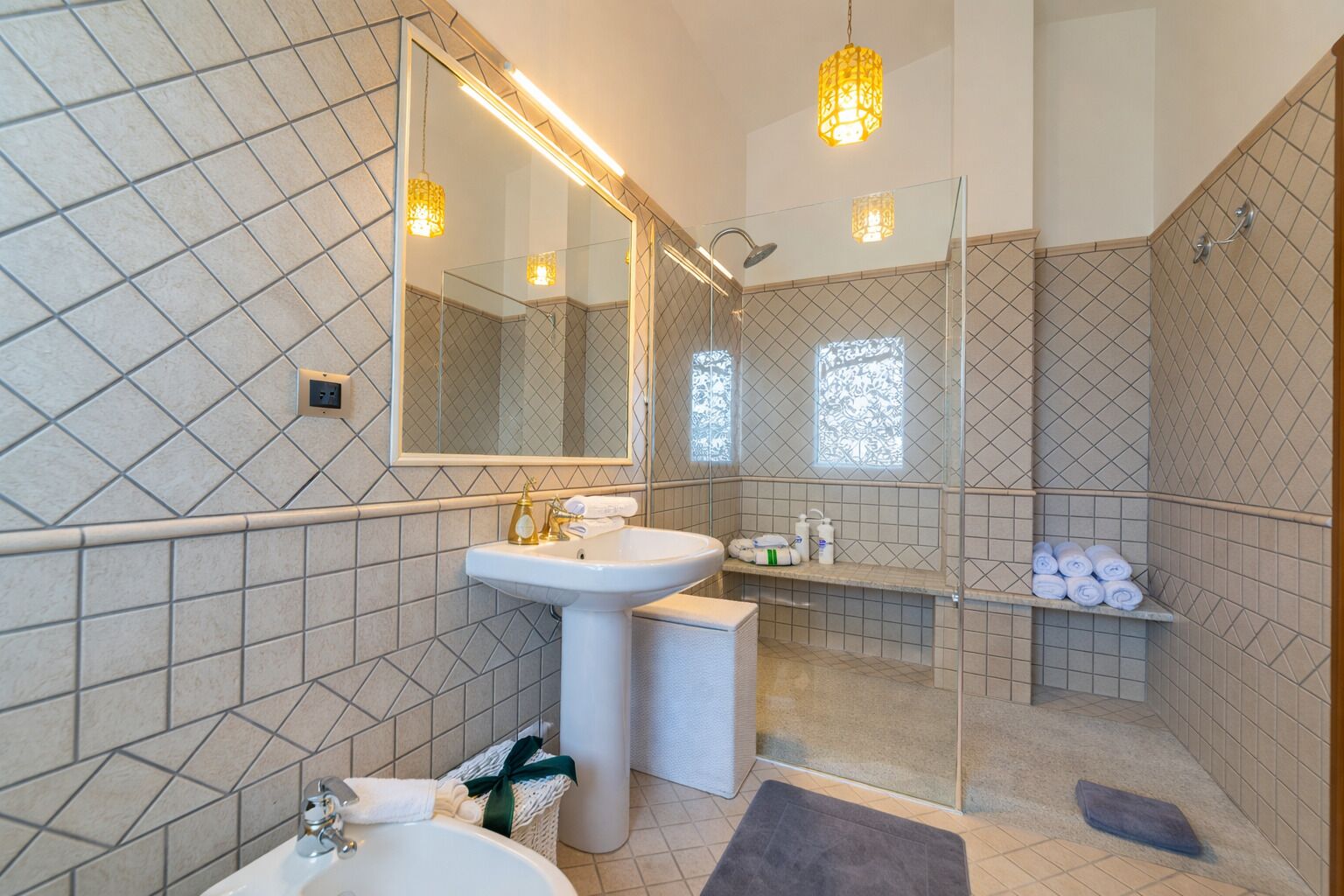 A modern bathroom with a large mirror, a pedestal sink, a shower enclosure, and a towel rack.