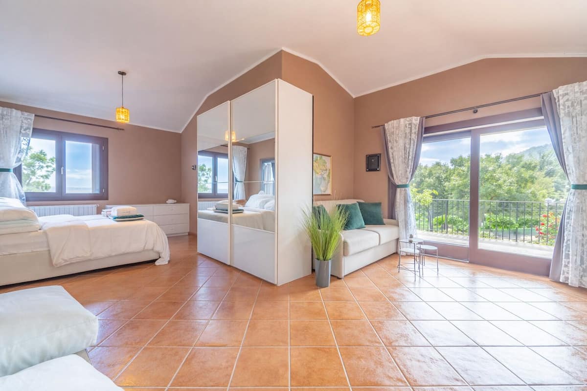 Un dormitorio con cama, sofá, mesita, planta en maceta y balcón con vistas.