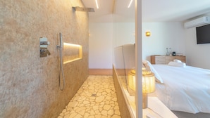 Una habitación de hotel moderna con ducha, cama, mesita de noche y televisor montado en la pared.