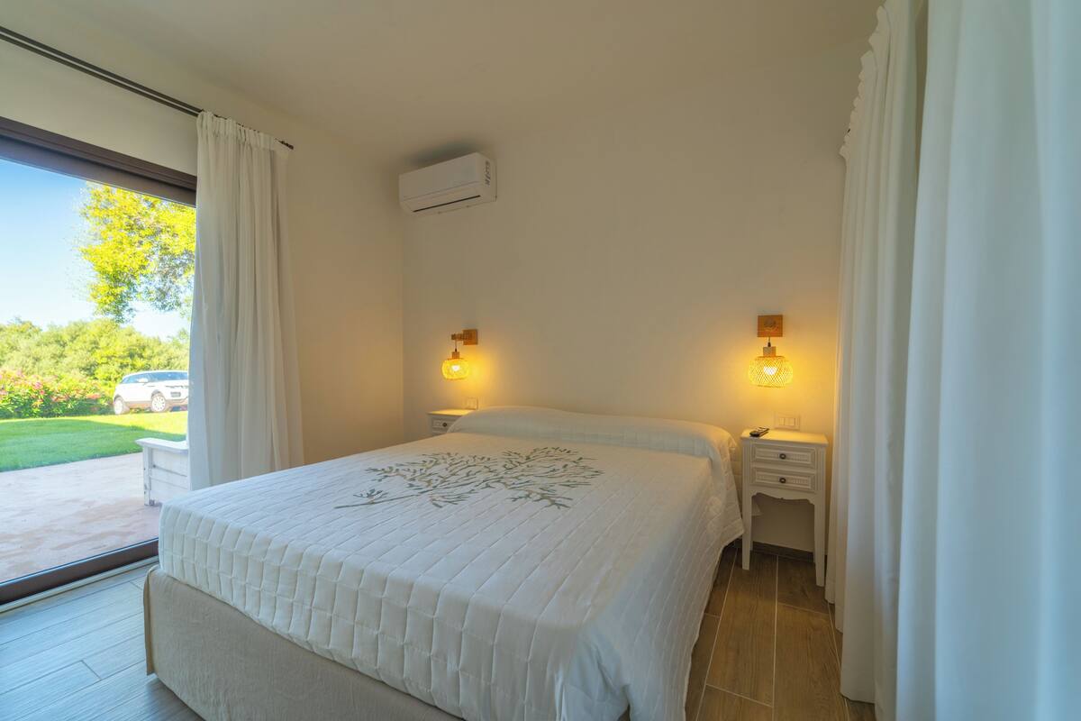 Un dormitorio con una cama grande, dos mesitas de noche, un equipo de aire acondicionado y vistas a un paisaje verde.